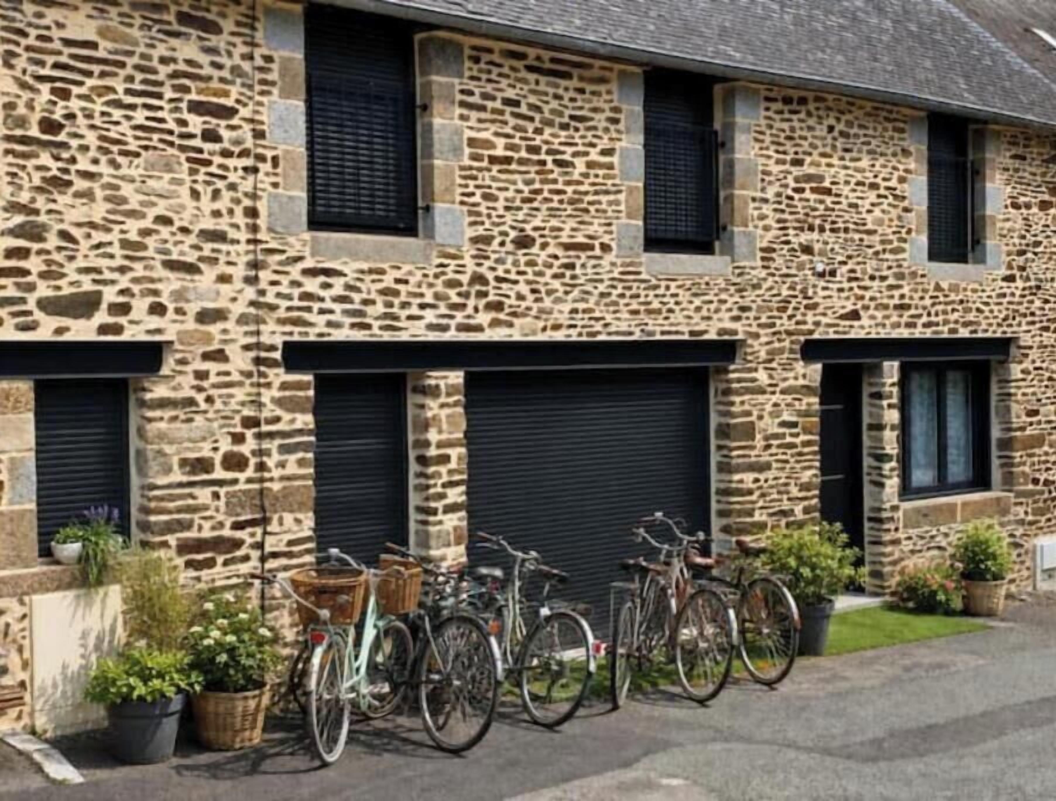 A stone building with multiple garage doors, bicycles parked in front, and potted plants.