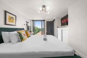 A hotel room with a bed, a television, and a view of the outside. - Knutsford Home | Sun Trap Garden | Sleeps 8 (Cheshire East)
