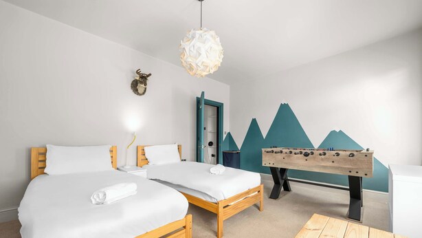 Habitación de hotel con dos camas, mesa de fútbol de madera, decoración de cabeza de animal en la pared y un diseño geométrico único en la pared.