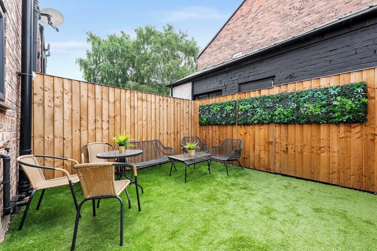 Un patio con cerramiento de madera, césped artificial verde y mobiliario exterior.