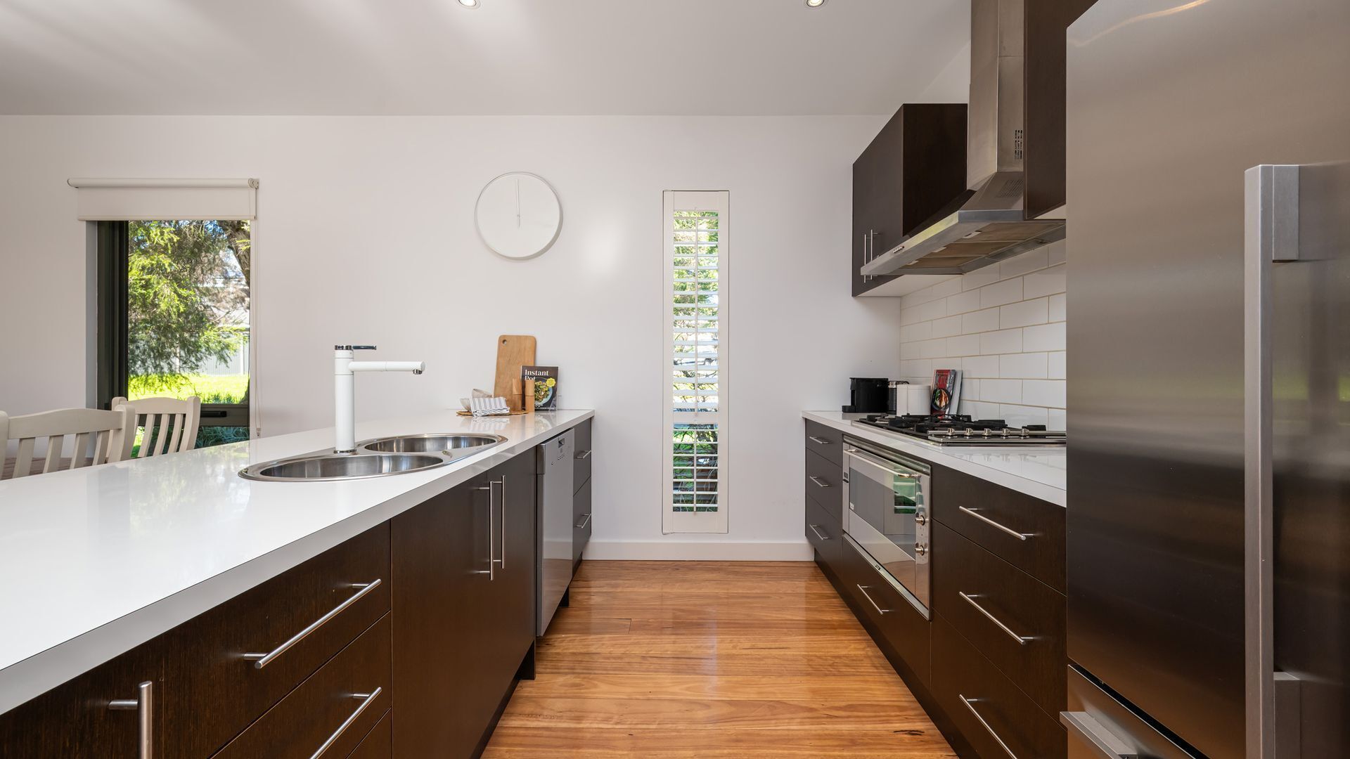 A modern kitchen with a central island, stainless steel appliances, and a view of greenery through a window.
