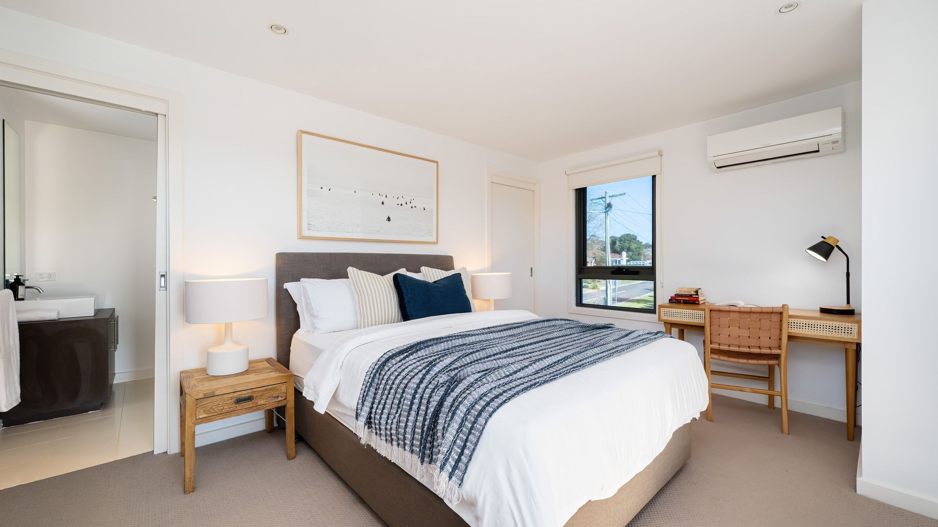 A modern bedroom with a bed, bedside tables, a desk, and an air conditioning unit.