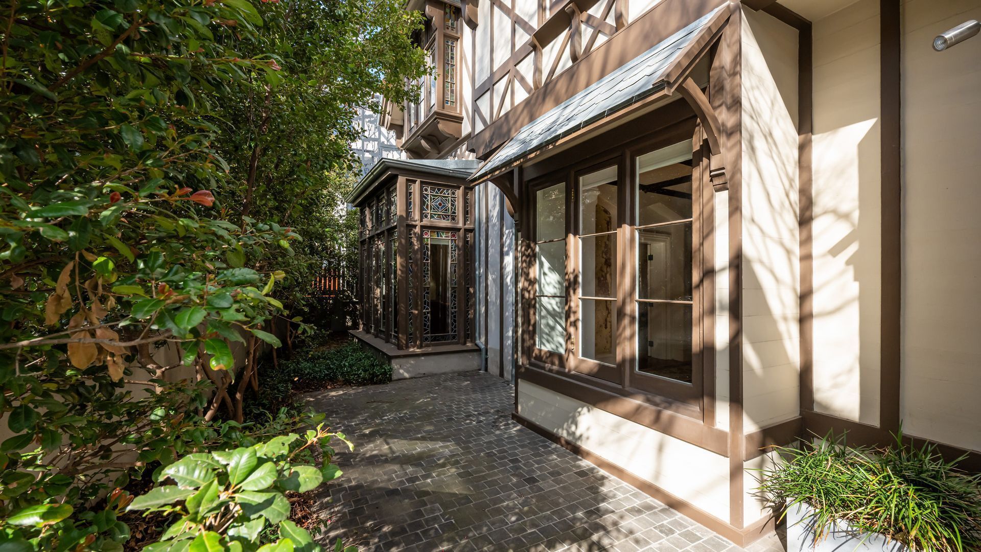A narrow pathway leading to a building with a traditional facade, a small garden area, and a window with a view.