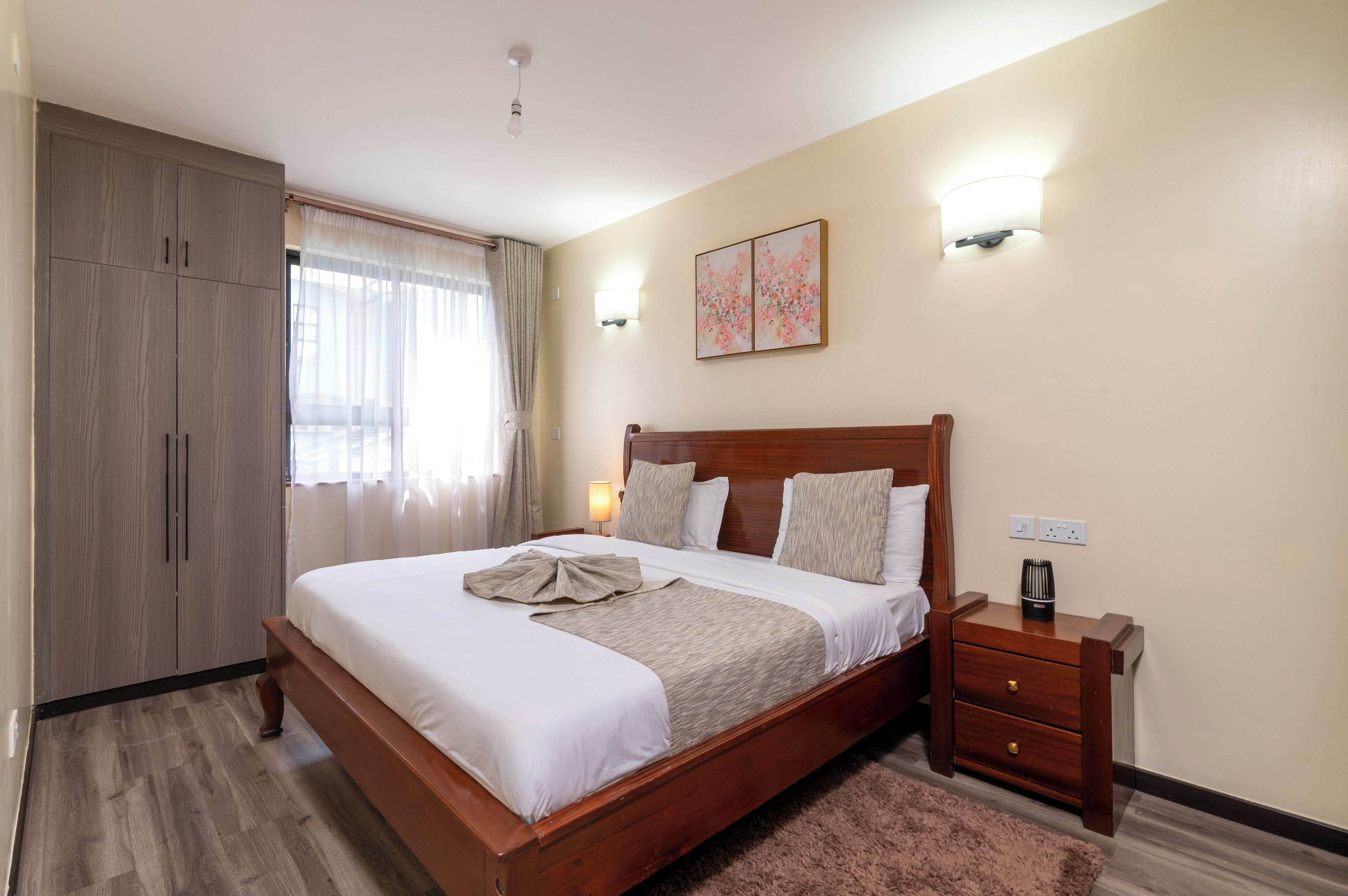 A hotel room with a wooden bed, a nightstand, a wardrobe, and a painting on the wall.