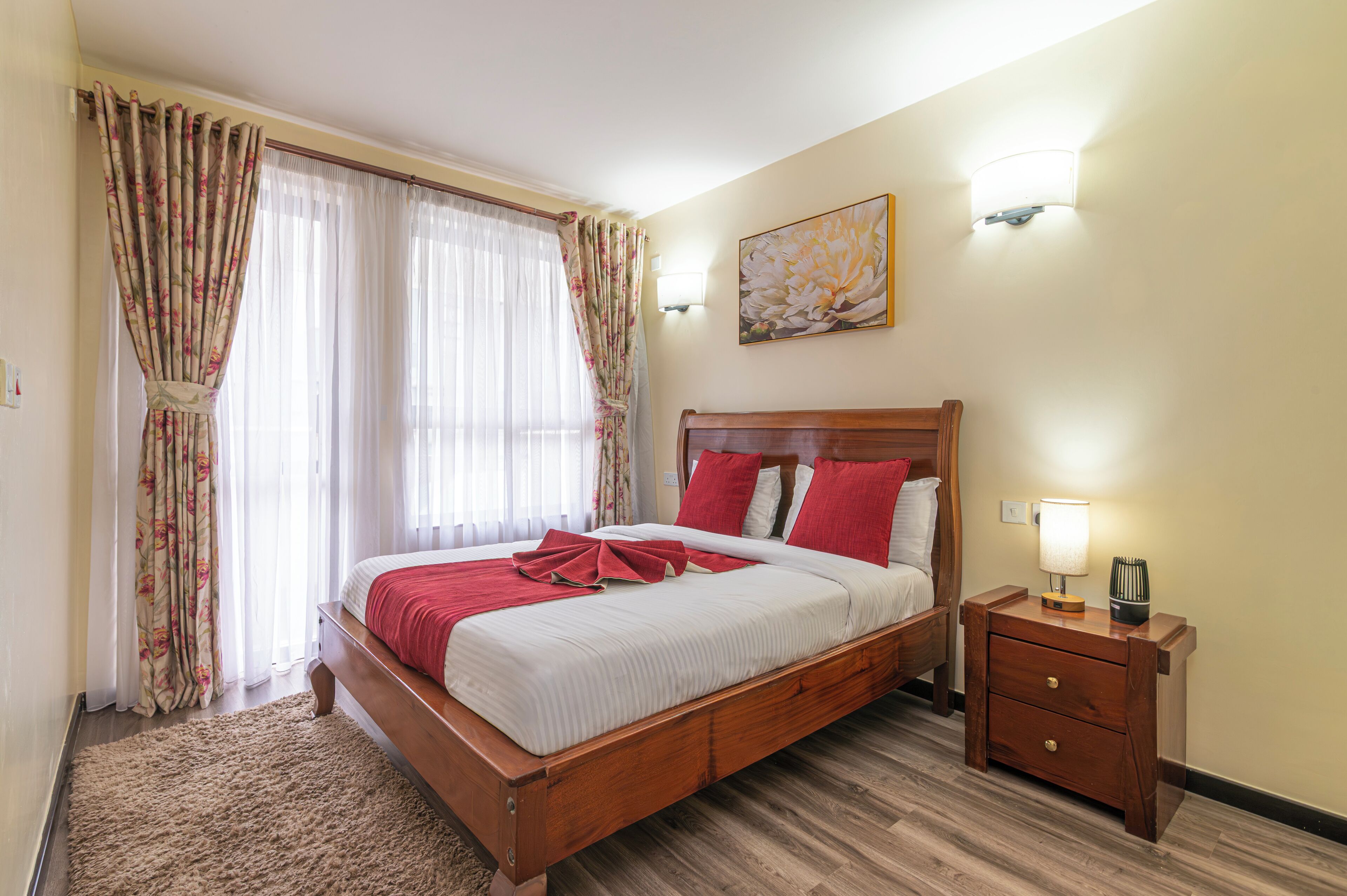 A hotel room with a wooden bed, a nightstand, a lamp, and a painting on the wall.