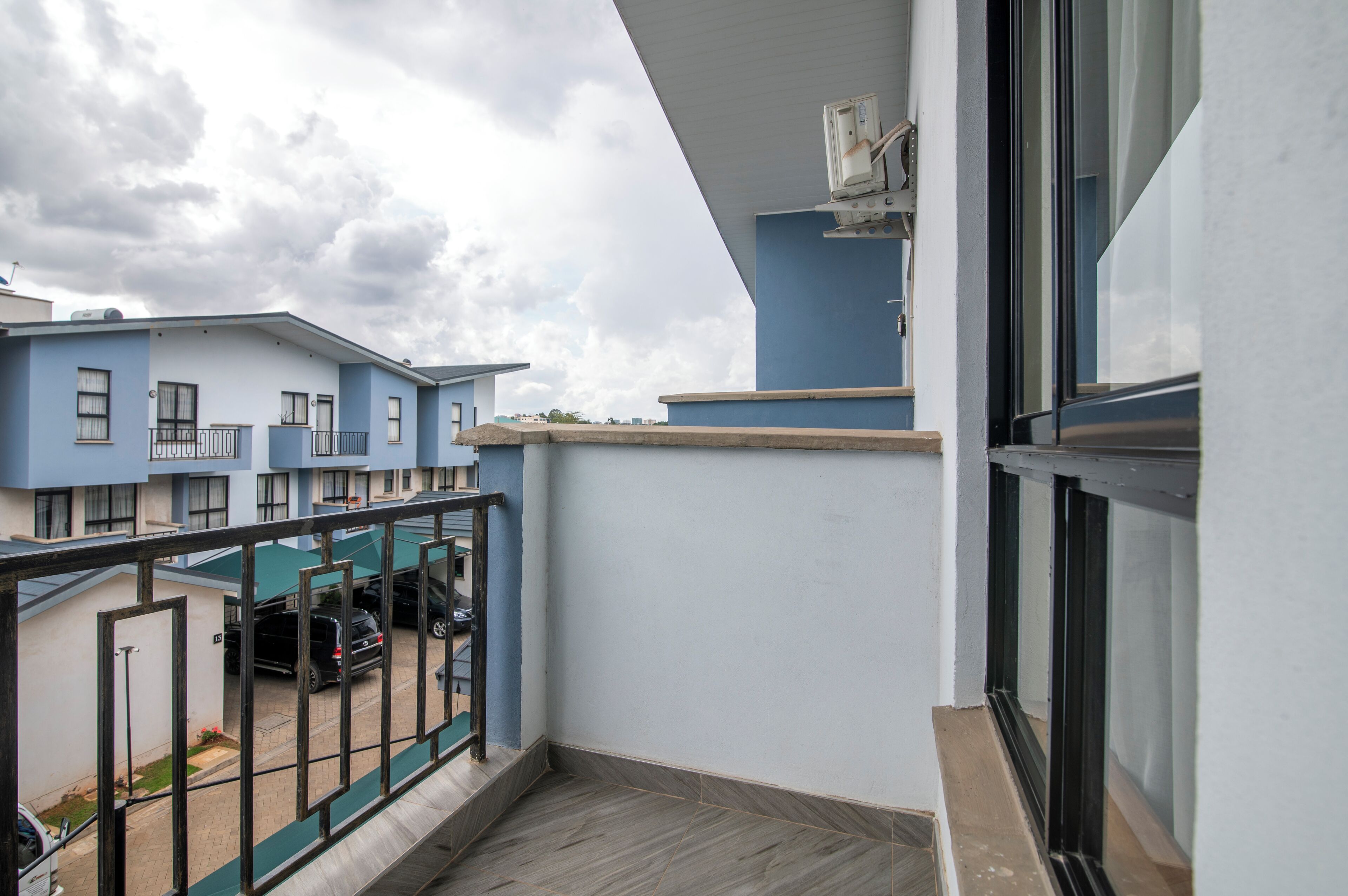 A balcony with a view of neighboring buildings and parked cars.