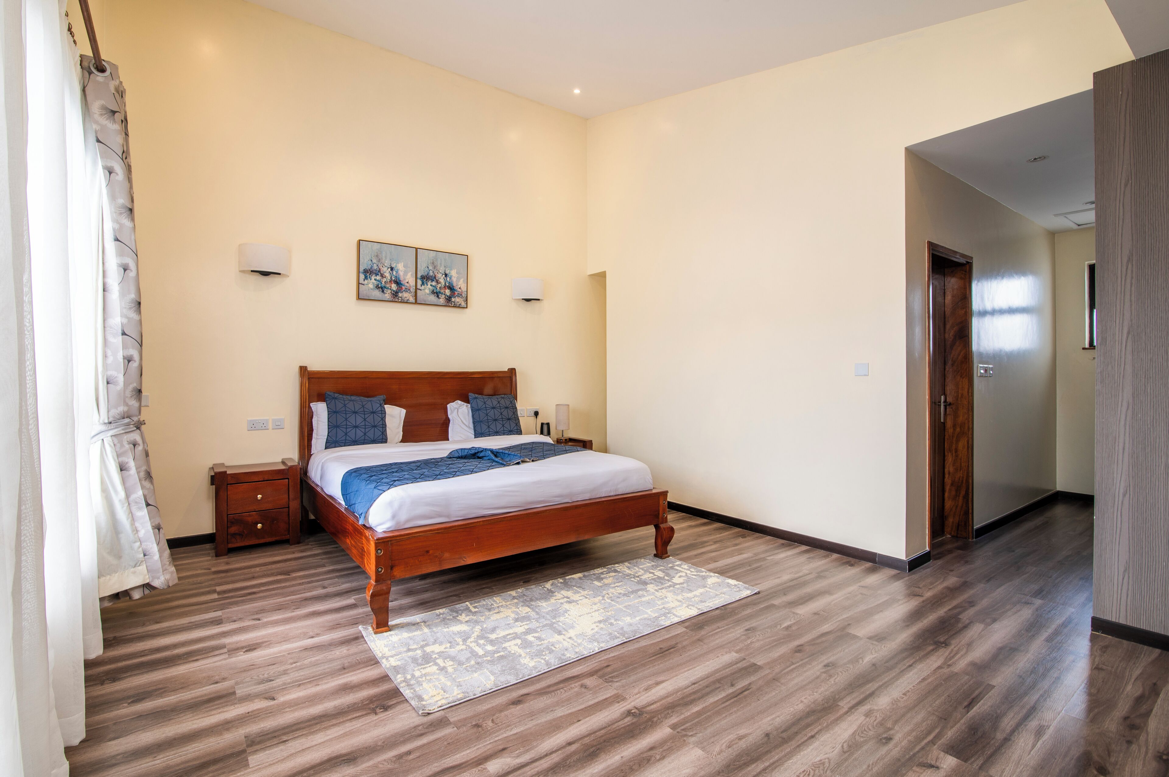 A bedroom with a wooden bed, a nightstand, a wall-mounted lamp, and a painting.