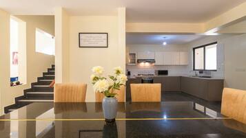 A modern kitchen with a dining area, featuring a marble table, a vase with flowers, and a framed quote on the wall.