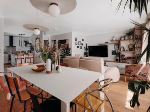 A modern kitchen with a dining area, a living room with a sofa and TV, and a bookshelf with various items. - Villa GIOIA Biarritz (Biarritz)