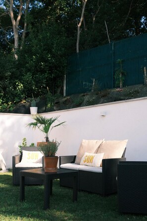 An outdoor seating area with wicker furniture, a potted plant, and a wall with a 'SUN' sign. - Villa GIOIA Biarritz (Biarritz)