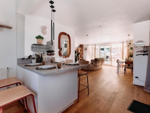 A modern kitchen with a central island, a dining area with a round table, and a living room with a sofa and a large window. - Villa GIOIA Biarritz (Biarritz)