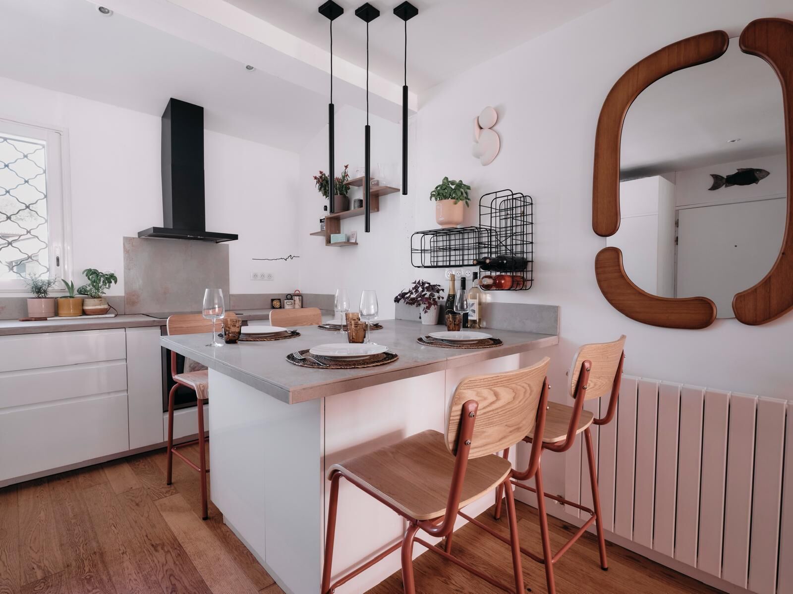 Una cocina moderna con una isla central, sillas de madera, lámparas colgantes y un espejo grande.