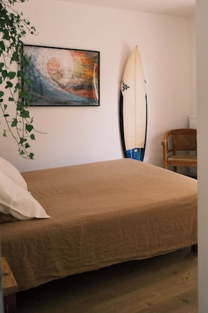 A bedroom with a bed, a chair, a surfboard, and a painting on the wall. - Villa GIOIA Biarritz (Biarritz)