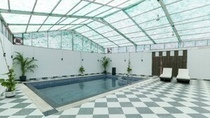 Una piscina interior amb un paviment a quadres, envoltada de parets amb plantes en testos i un sostre de vidre.