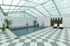 An indoor swimming pool with a checkered floor, surrounded by walls with potted plants, and a glass ceiling. - Chaubeyji's Heritage Hotel (Bah)