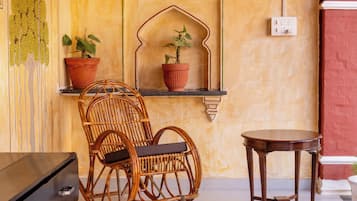 A room with a wicker chair, two potted plants, a small table, and a black dresser.