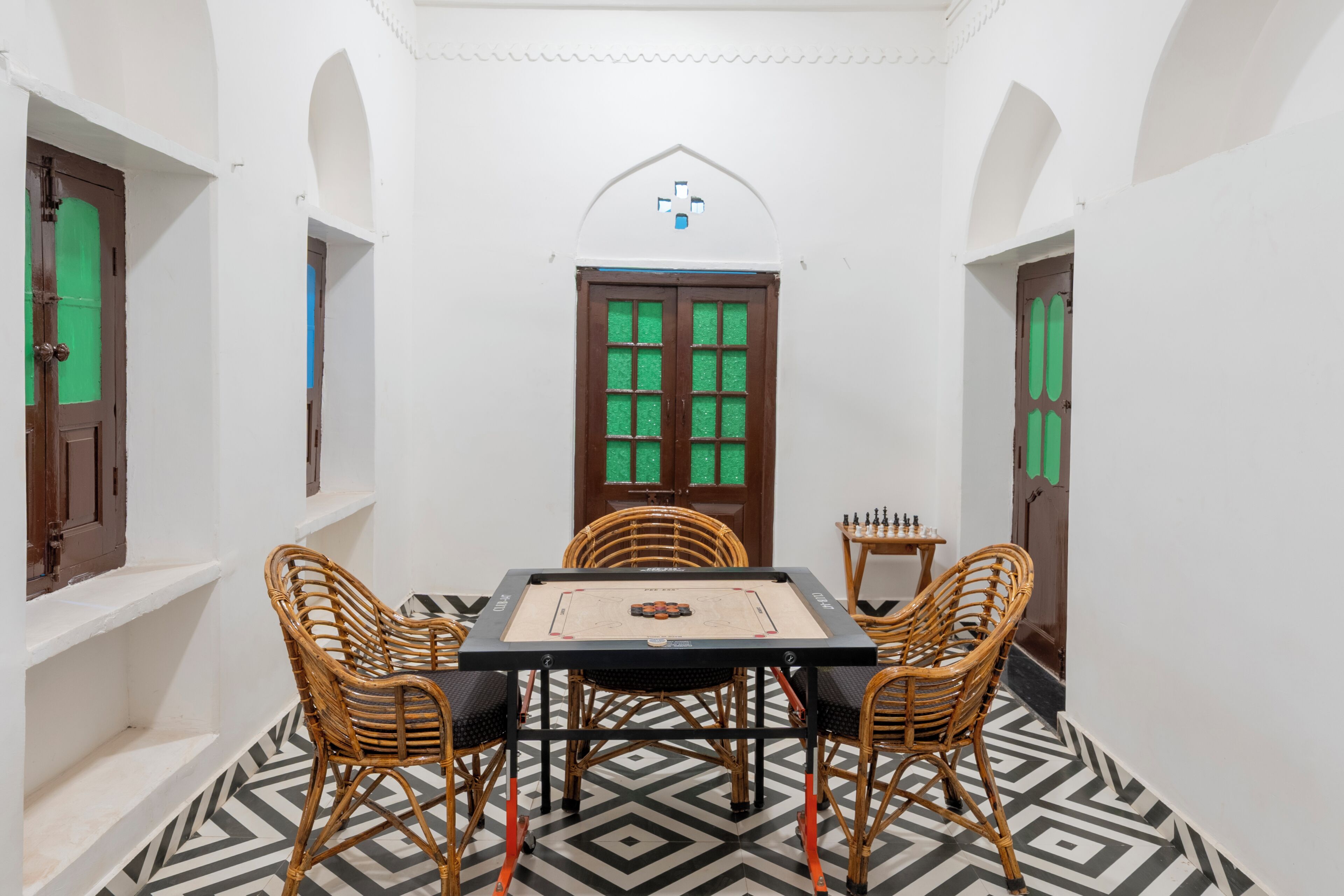 A room with a chessboard, two wicker chairs, a table, and a door with green glass panels.