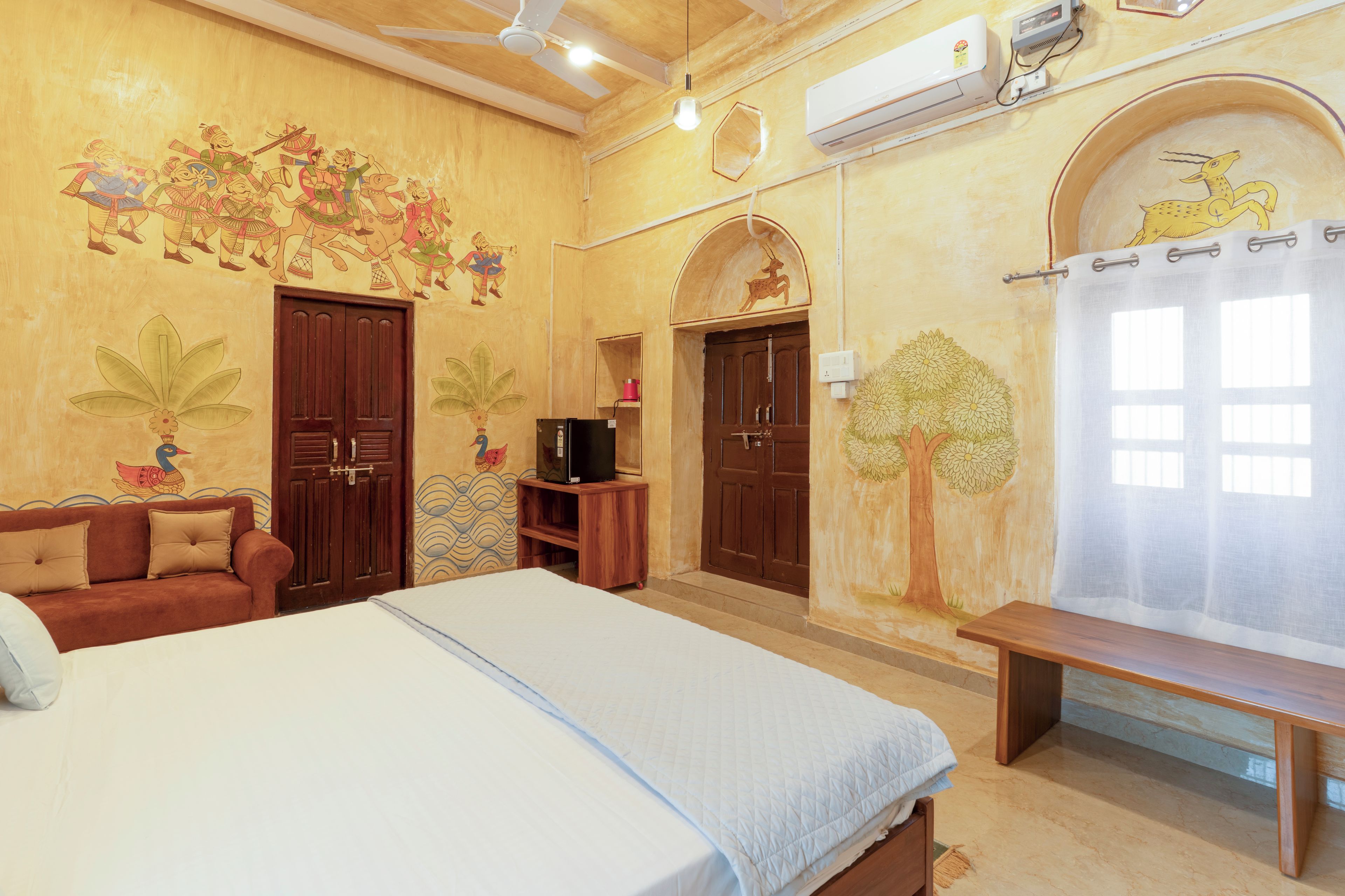 Una habitación con cama, sofá, mueble para televisión y una pared decorada con arte tradicional.