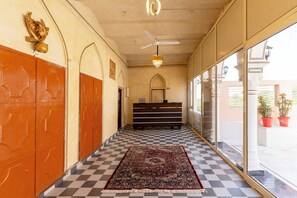 A hotel corridor with a checkered floor, a reception desk, and a large window with potted plants.