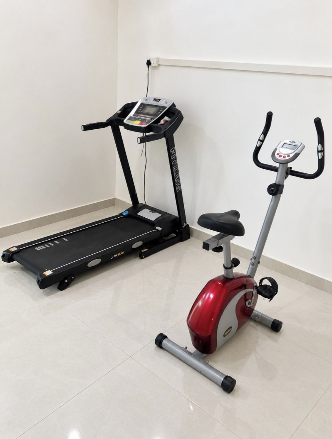 Una caminadora y una máquina elíptica en una sala con piso de baldosas y pared blanca.
