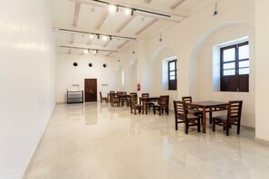 A spacious room with a high ceiling, a dining area with wooden tables and chairs, and large windows allowing natural light. - Chaubeyji's Heritage Hotel (Bah)