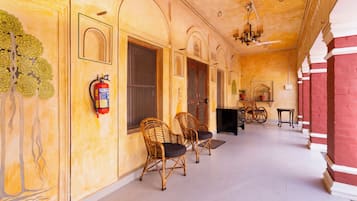 A corridor with a fire extinguisher mounted on the wall, wicker chairs, and a piano.