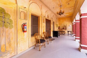 A corridor with a fire extinguisher mounted on the wall, wicker chairs, and a piano.