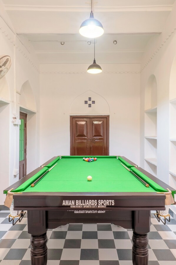 A pool table with a green felt surface, a white ceiling with a hanging light fixture, and a wooden door with a small window.