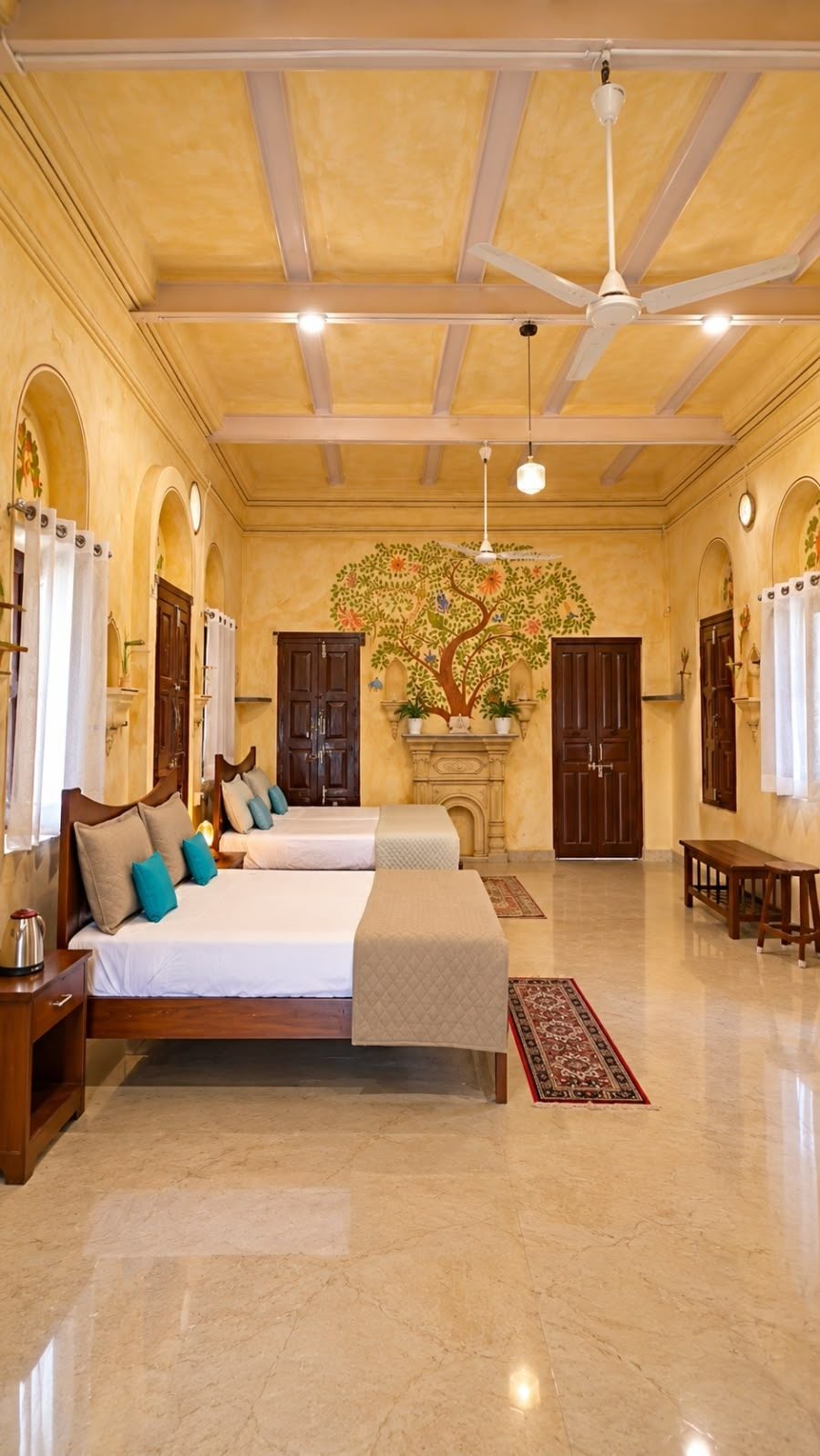 Une chambre d’hôtel spacieuse, dotée d’un grand lit, de deux tables de chevet, d’un ventilateur de plafond et d’une fresque murale représentant un arbre décoratif.