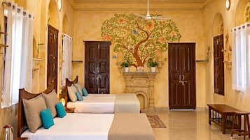 Une chambre d’hôtel spacieuse, dotée d’un grand lit, de deux tables de chevet, d’un ventilateur de plafond et d’une fresque murale représentant un arbre décoratif.