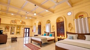 A hotel room with two beds, a sofa, a TV, and decorative wall art. - Chaubeyji's Heritage Hotel (Shikohabad)