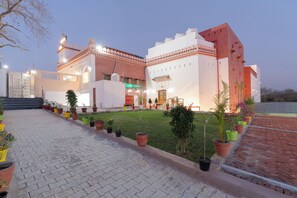 A building with a paved entrance, a well-maintained lawn, and a variety of potted plants. - Chaubeyji's Heritage Hotel (Bah)