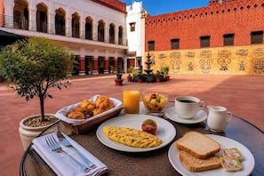 Una escena de desayuno con una mesa, comida y vista a un patio con edificios.