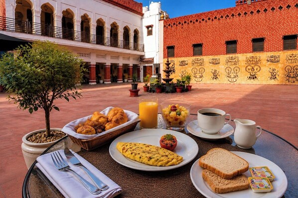 A breakfast setting with a table, food, and a view of a courtyard with buildings. - Chaubeyji's Heritage Hotel (Bah)