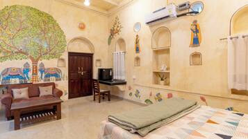 A room with a large mural, a bed with a patterned bedspread, a wooden bench, and a wall-mounted air conditioning unit.