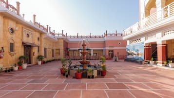 A courtyard with a central fountain, potted plants, and a mural on the wall.