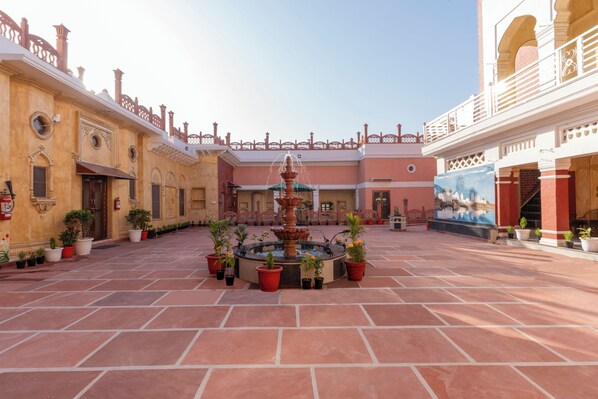 A courtyard with a central fountain, potted plants, and a mural on the wall.