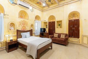 A hotel room with a bed, a sofa, a TV, and decorative wall art. - Chaubeyji's Heritage Hotel (Bah)