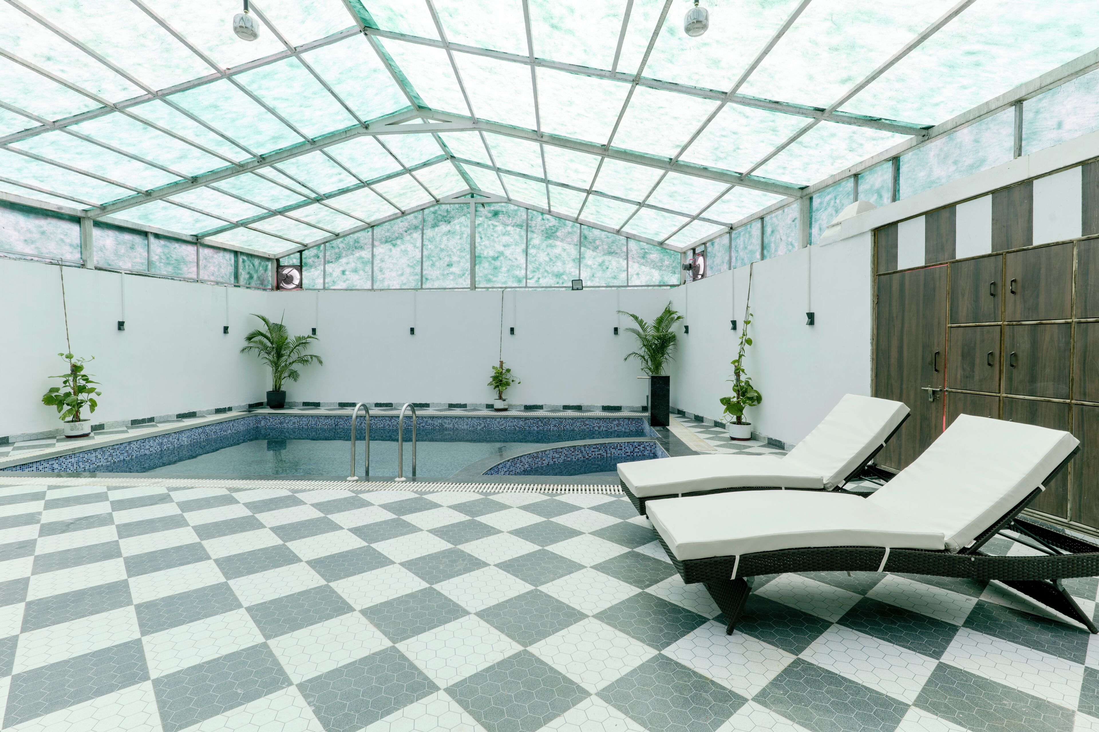 An indoor swimming pool with checkered flooring, lounge chairs, and potted plants.
