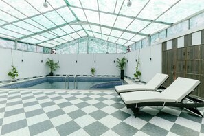 An indoor swimming pool with checkered flooring, lounge chairs, and potted plants.
