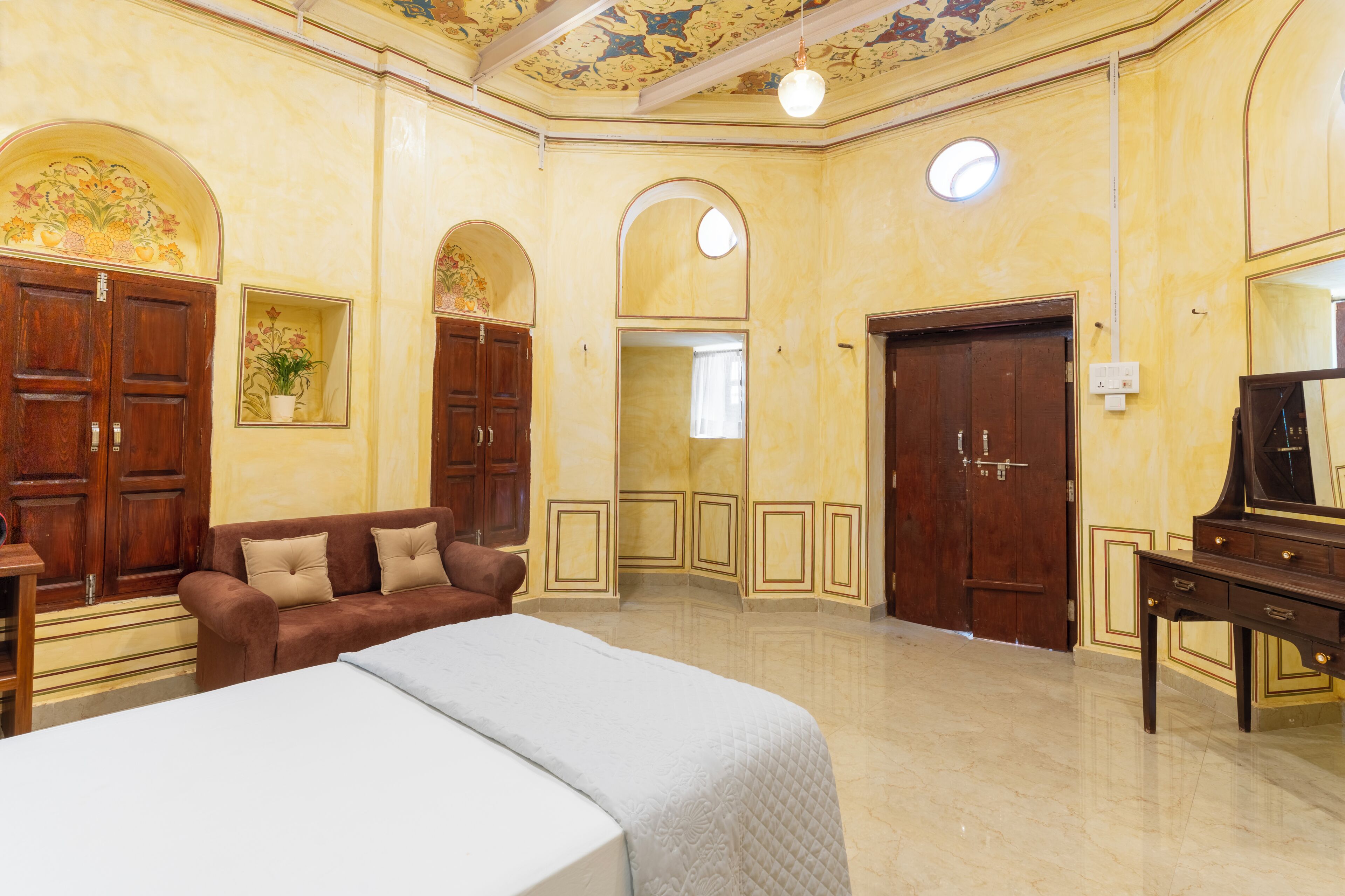 A hotel room with a large bed, a sofa, a desk, and a piano. There are two doors and a window.