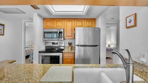 A modern kitchen with a skylight, stainless steel appliances, granite countertops, and wooden cabinets. - Midnight Cove II – Unit 513 - Pool View! (Siesta Key)