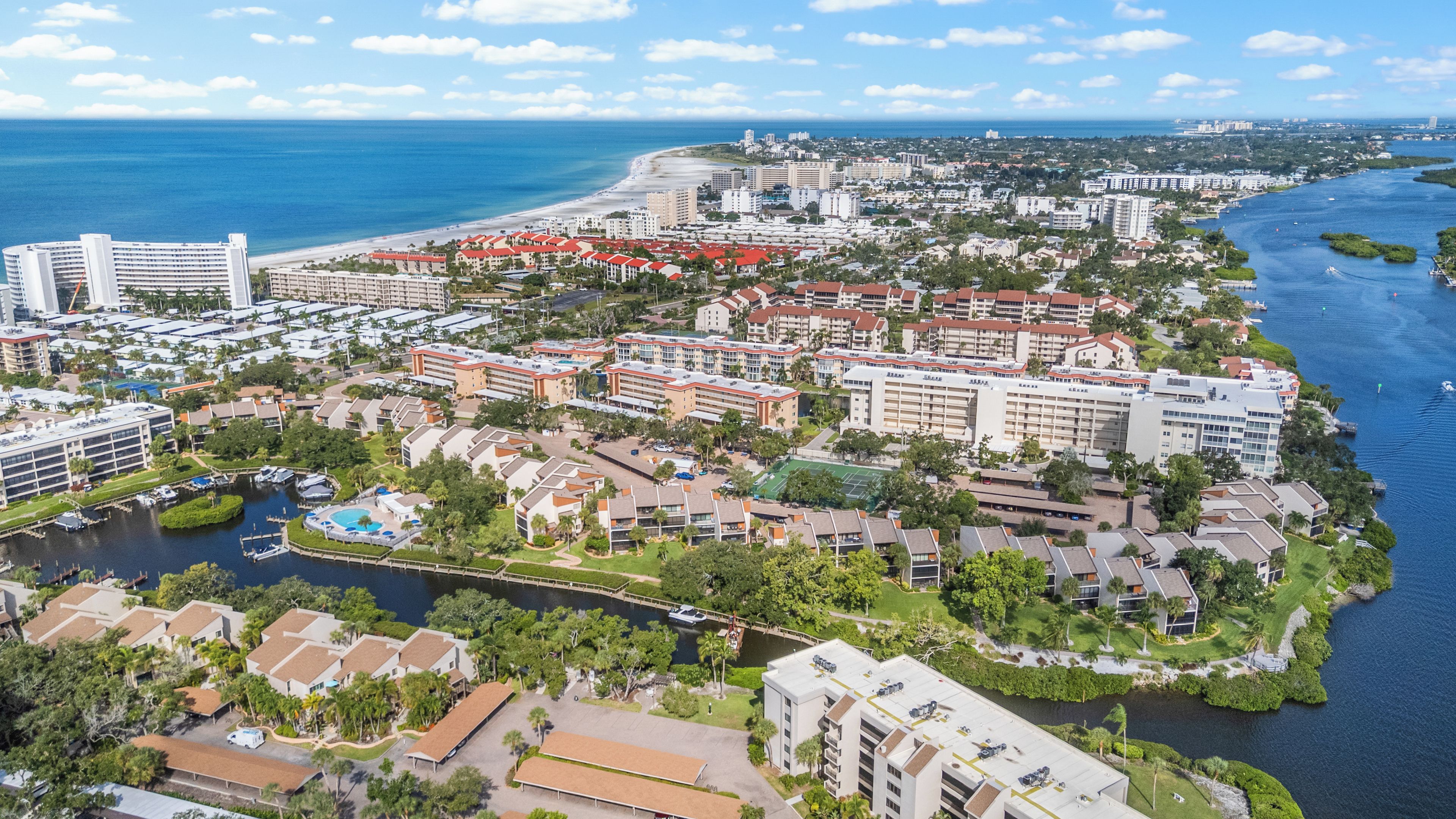 Un complejo turístico frente al mar con varias edificaciones, un puerto deportivo y una playa.