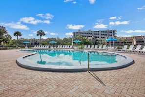 A swimming pool with lounge chairs and umbrellas, surrounded by a brick patio and palm trees. - Midnight Cove II – Unit 513 - Pool View! (Siesta Key)