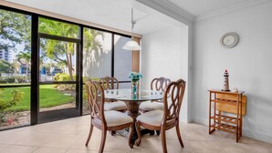 A dining area with a glass table, wooden chairs, a vase with flowers, and a small wooden side table with a lighthouse model. - Midnight Cove II – Unit 513 - Pool View! (Siesta Key)