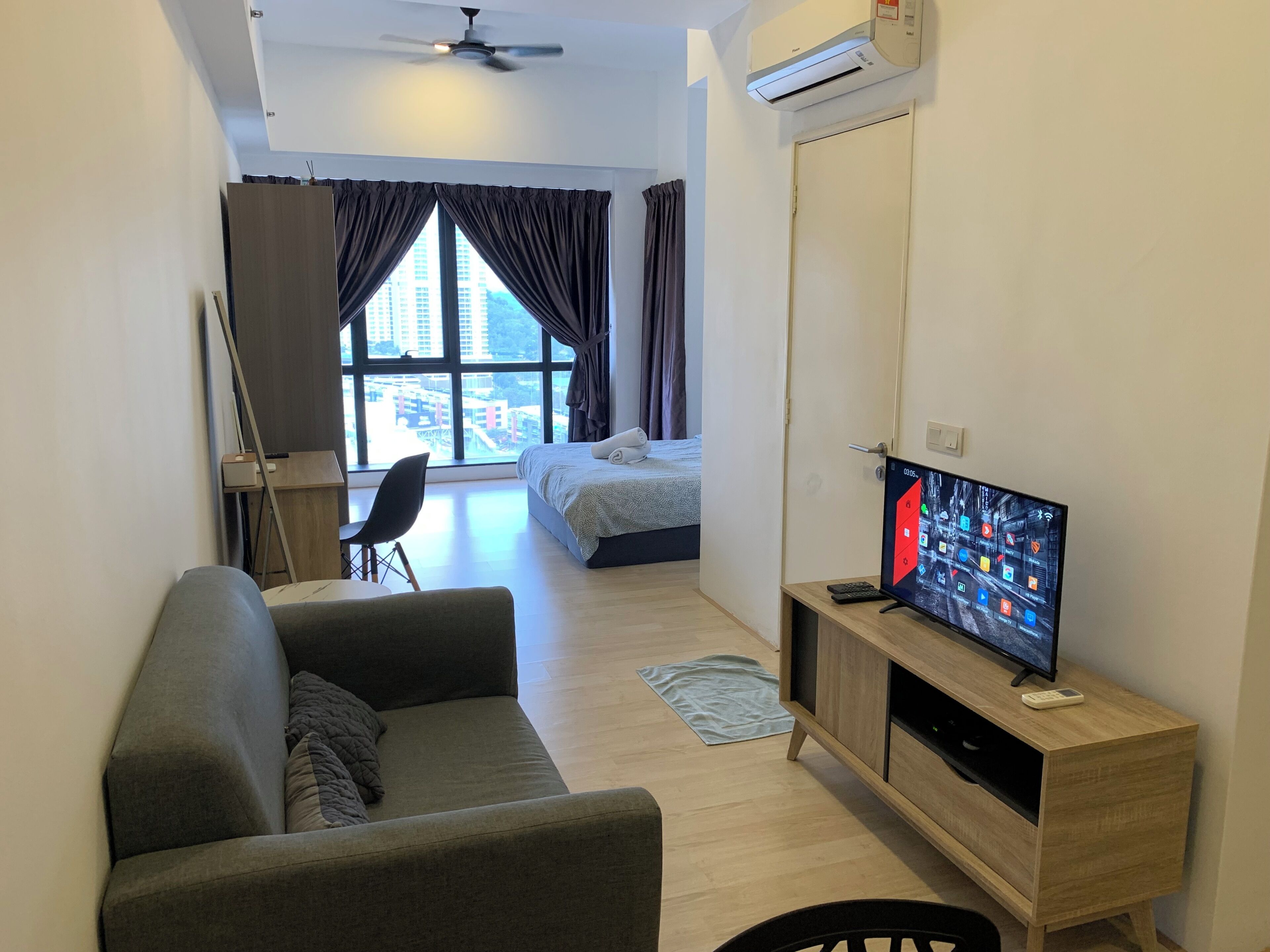 Una sala de estar moderna con un sofá, un televisor sobre un mueble de madera y un amplio ventanal con cortinas.