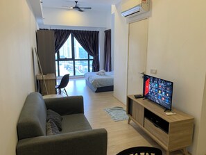 A modern living room with a sofa, a TV on a wooden stand, and a large window with curtains.