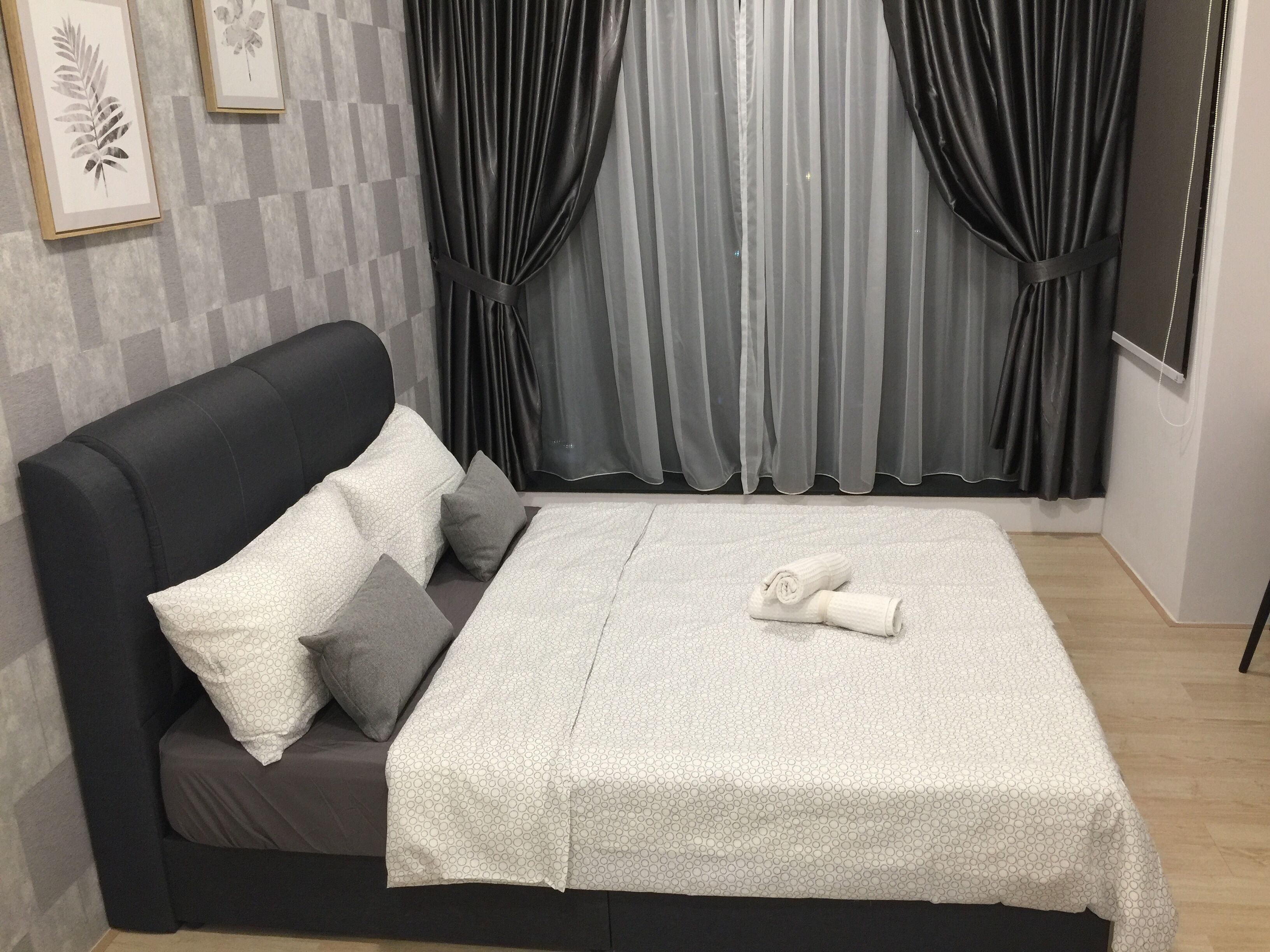 A bed with a white blanket, two pillows, and a rolled towel.