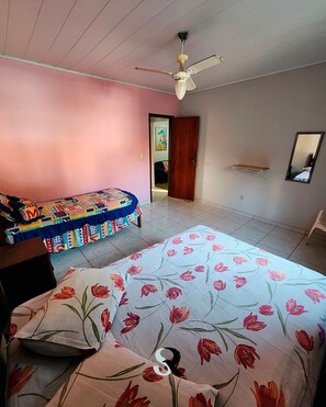 A bedroom with a bed, a colorful sofa, a ceiling fan, a door, and a mirror on the wall.