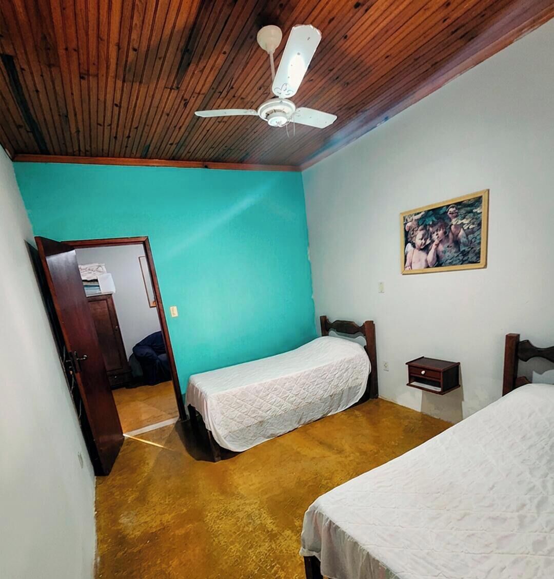 Una habitación con techo de madera, ventilador de techo, cama con cubrecama blanco, mesita de noche y un cuadro en la pared.